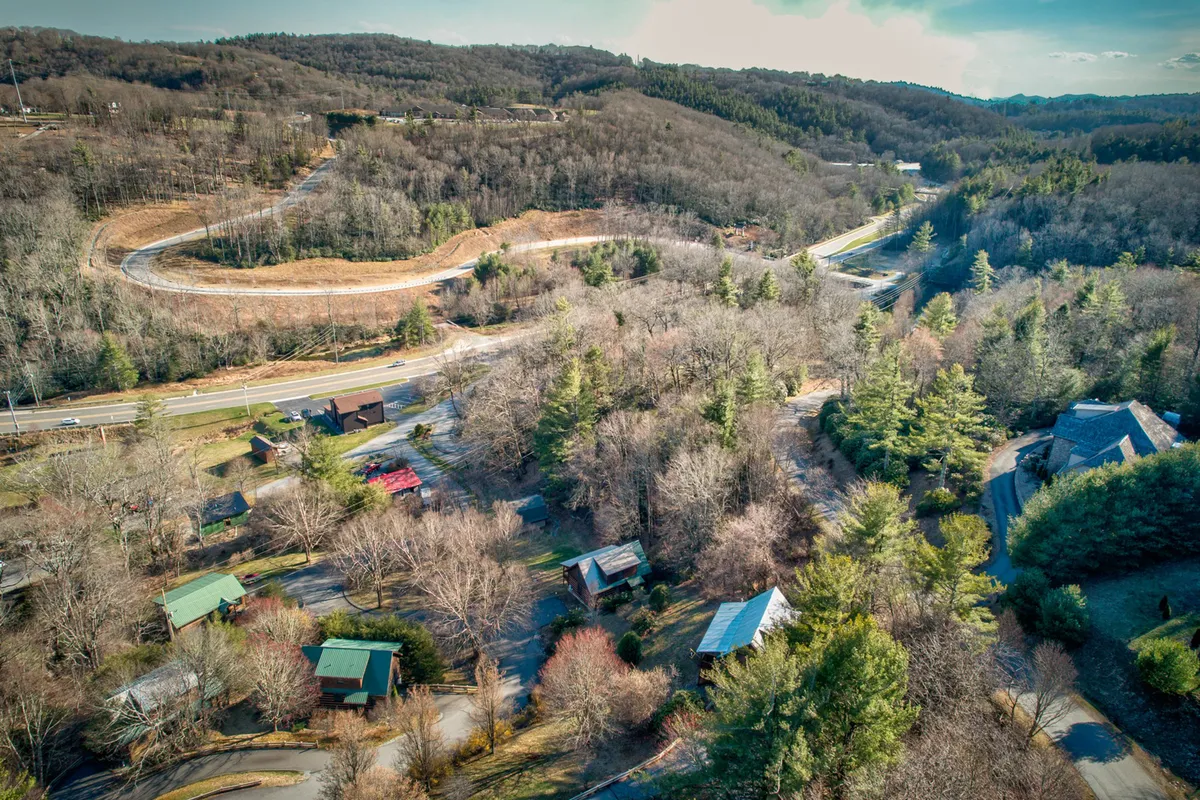 A panoramic view of a winding road weaving through a dense forest, with scattered cabins and a meandering river visible in the landscape. The natural surroundings evoke the serenity and grandeur of the High Country.