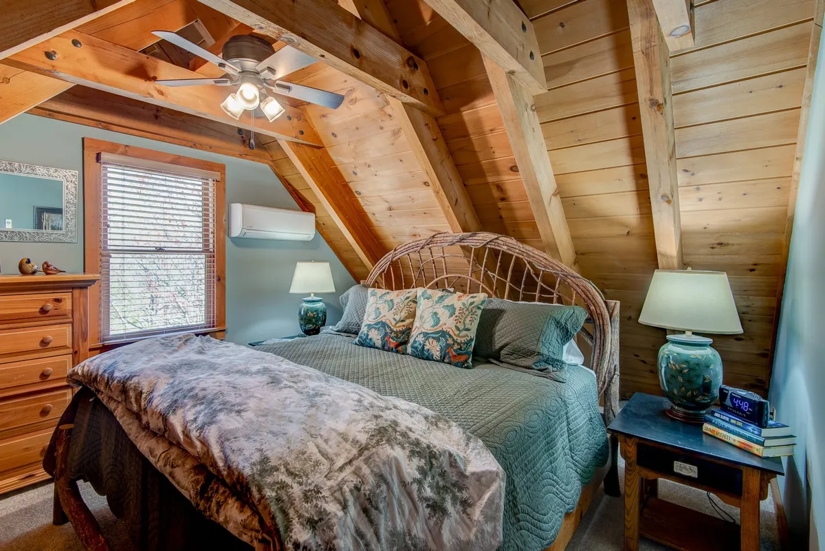 A tranquil bedroom accented with wooden ceiling beams, a bed adorned with decorative pillows, and a nightstand with a warm lamp. The cozy setup and soft lighting promote relaxation and comfort.