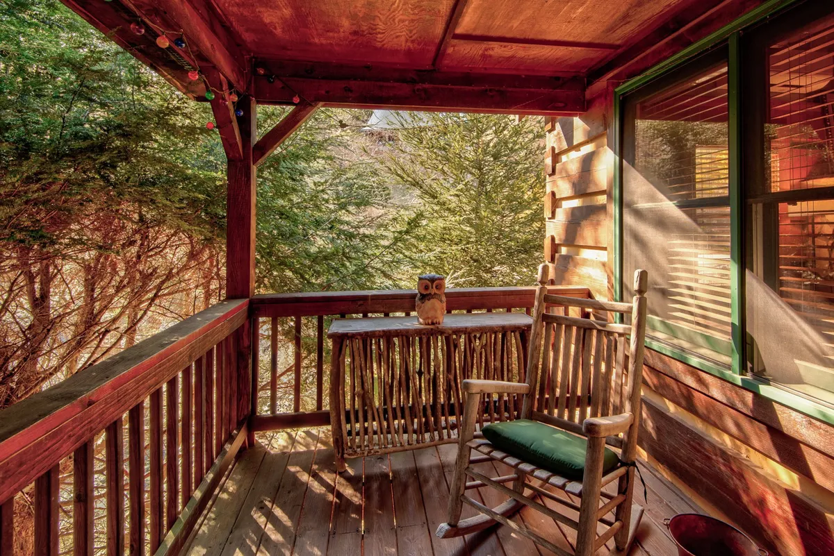 A peaceful exterior shot focusing on a rocking chair and wooden table on the porch, accented by owl decor and vibrant greenery. The inviting setup is perfect for enjoying nature, quiet mornings, or stargazing together in serene privacy.
