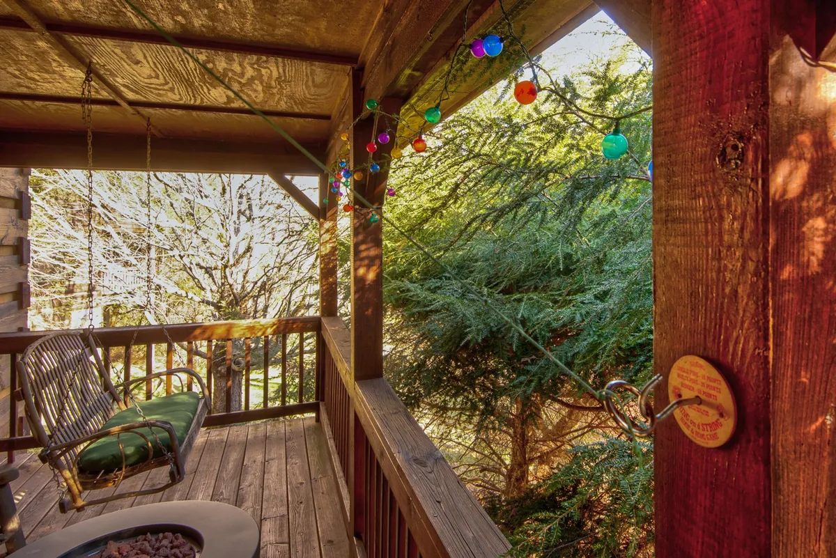 A cheerful outdoor scene with hanging colored lights, a wooden swing, and lush green foliage. The space feels cozy and connected to the surrounding nature, ideal for enjoying sunsets or gathering after a day of adventure.