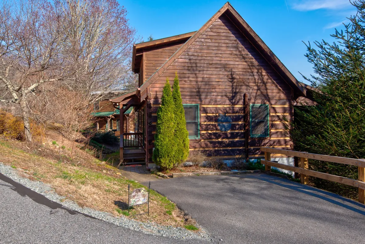 This exterior image highlights the charming wooden cabin nestled amid lush greenery, featuring a welcoming front porch and a stone pathway leading up to the entrance. The scene evokes a sense of arrival and connection to nature, with hints of family gatherings and outdoor relaxation.