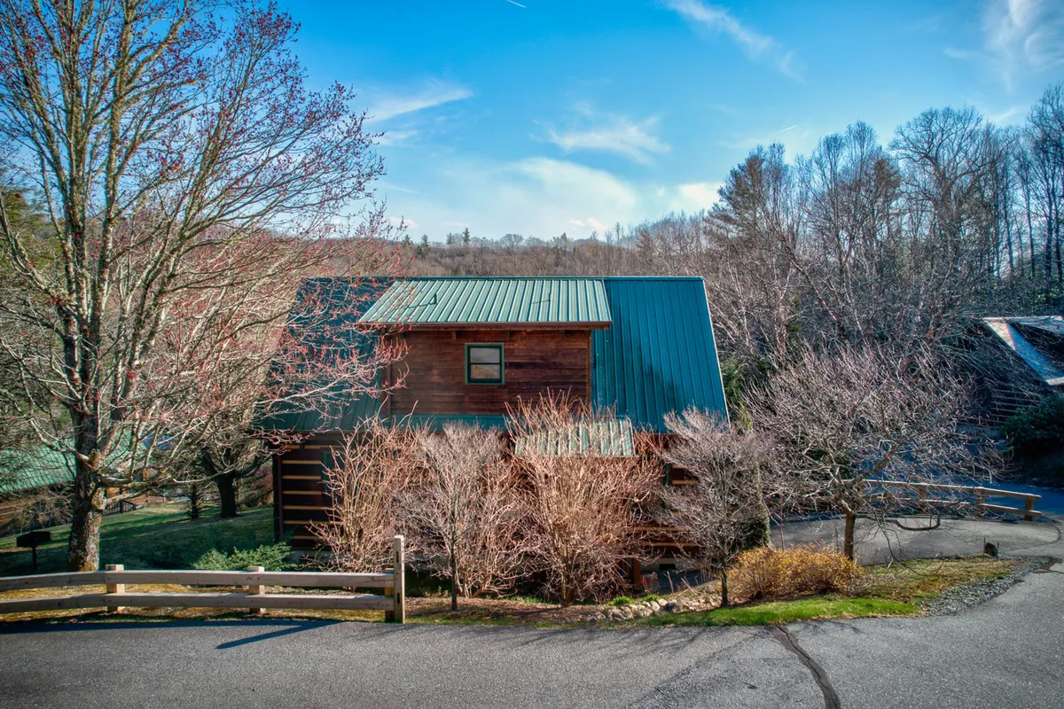 This image captures the wooden Apple Cabin nestled among lush trees, with a green metal roof and a winding driveway leading up to the entrance. The tranquil setting and natural surroundings evoke a sense of seclusion and relaxation. The cabin's porch is visible, inviting thoughts of morning coffee or evening wine while soaking in the quiet mountain atmosphere.